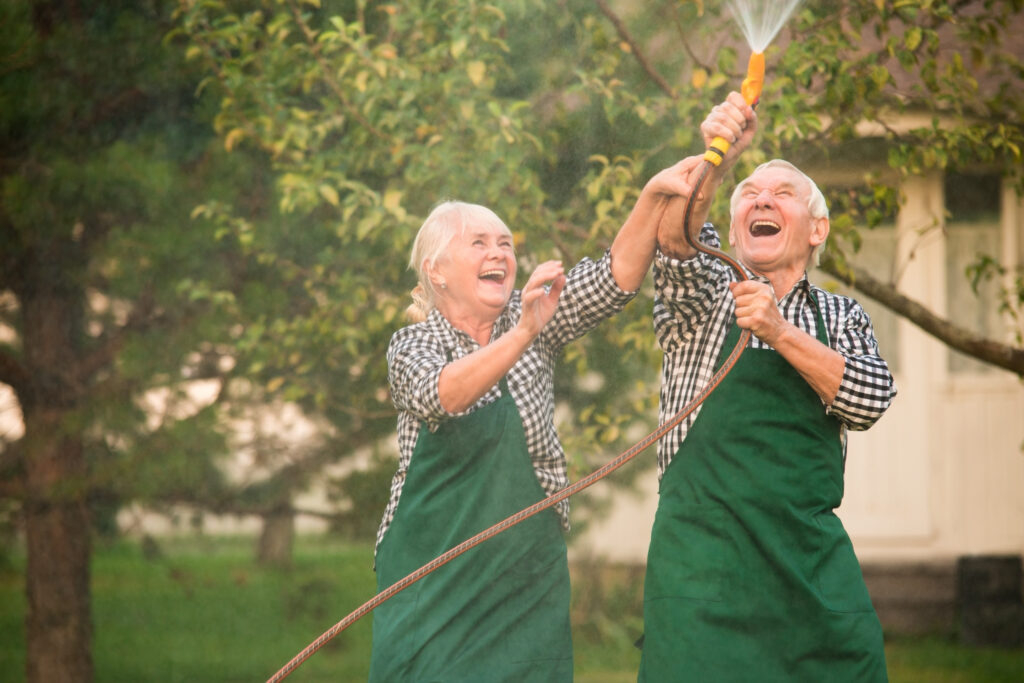 Fröhliches Seniorenpaar macht Spaß mit dem Gartenschlauch im Garten.