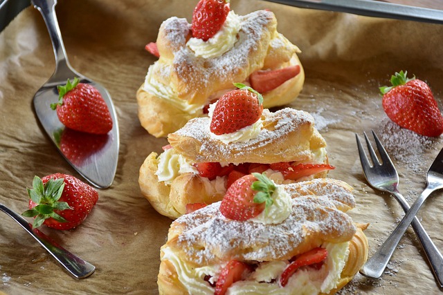 Drei köstliche Eclair mit Erdbeeren und Sahne, dekoriert mit Besteck, einem Kuchenschieben und erntefrischen Erdbeeren