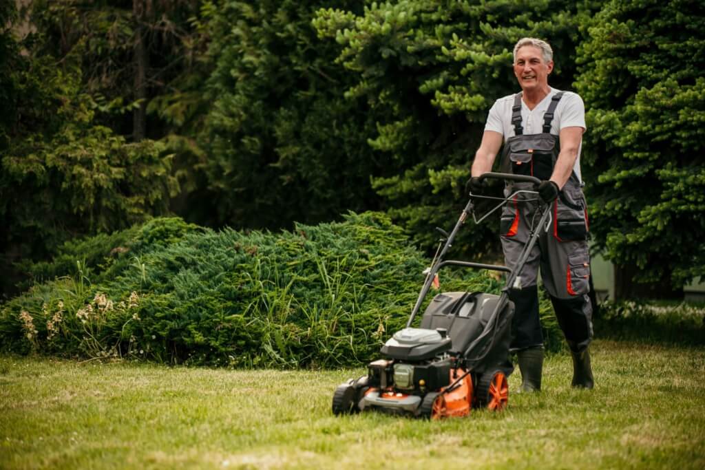 Ein älterer Hobbygärtner mäht seinen Rasen mit einem Benzin-Rasenmäher.