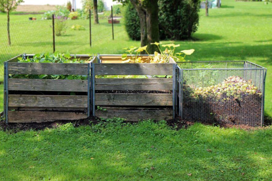 Ein teilweise gefüllter Drei-Kammer-Komposter steht auf einer Gartenwiese.