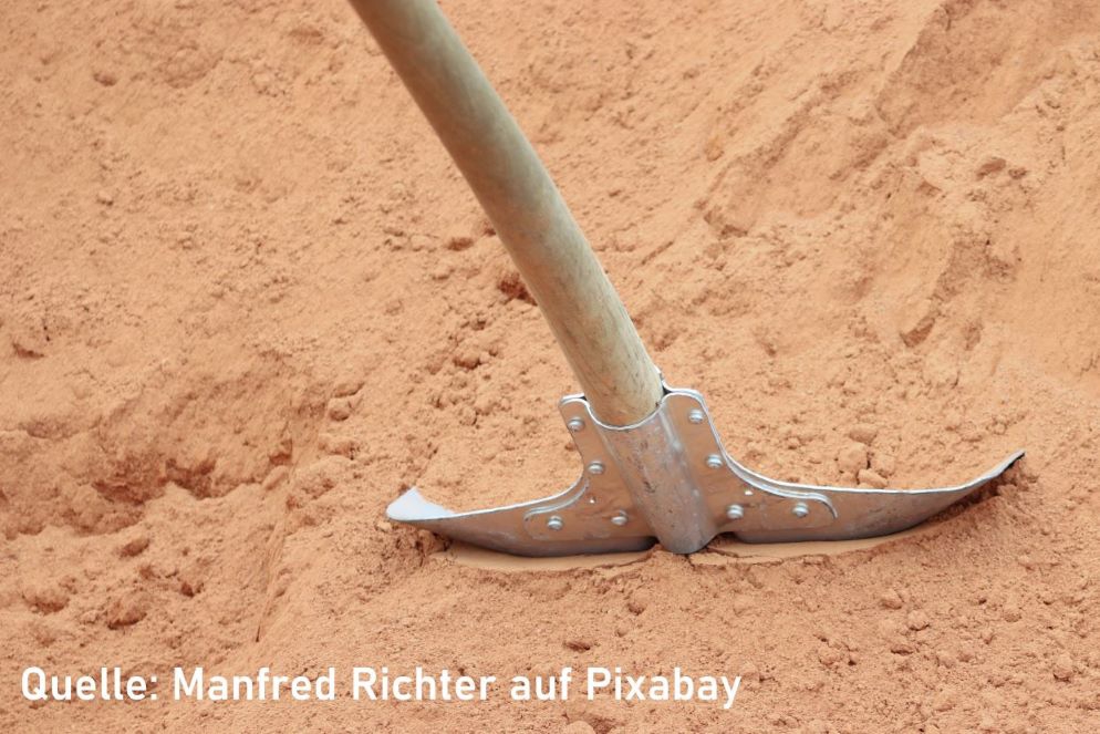 Eine Schaufel steckt in einem Sandhaufen, bereit für ihren nächsten Einsatz für die Verbesserung des Gartenbodens.