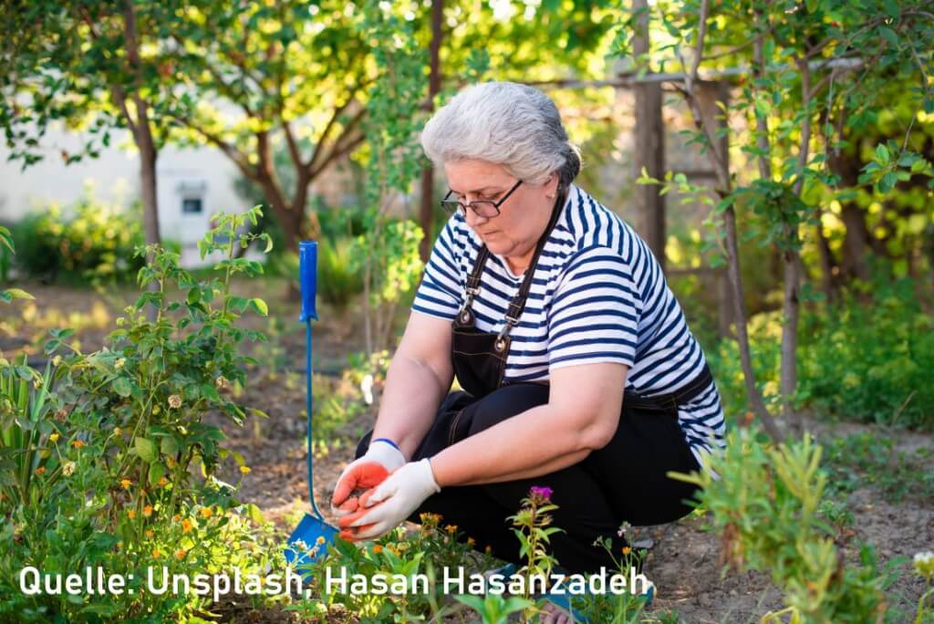 Eine Hobbygärtnerin50+ sitzt in der Hocke im Garten und pflanzt Blumen.