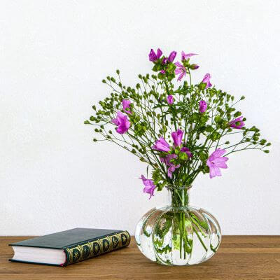 Ein Strauß aus Präriemalven steht in einer gläsernen Vase auf dem Tisch. Ein Buch liegt daneben