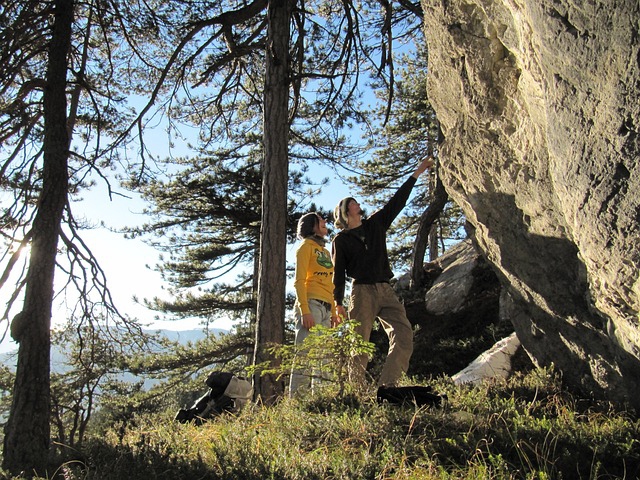 Bergwanderer abseits der Wanderwege stehen an einem Felsen unter Bäumen.