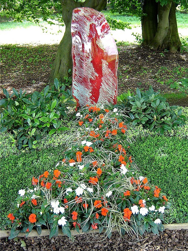 Ein kleines Grab mit Edellieschen und anderen Pflanzen und einem rötlichen Grabstein.