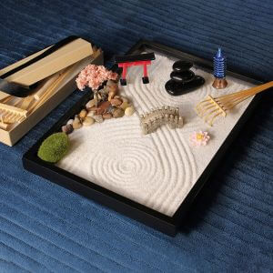 Auf einem blauen Teppich steht eine Zen Garten Mini mit allen Accessoires.